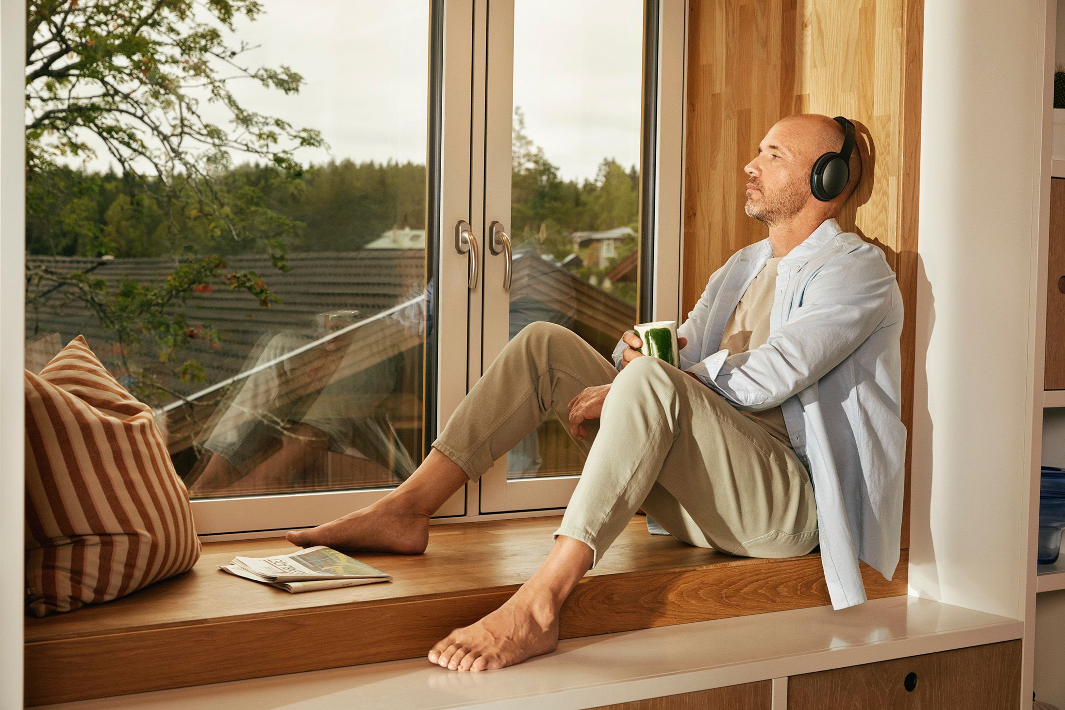 Mann som sitter i vinduskarmen med kaffekoppen og hodetelefoner på