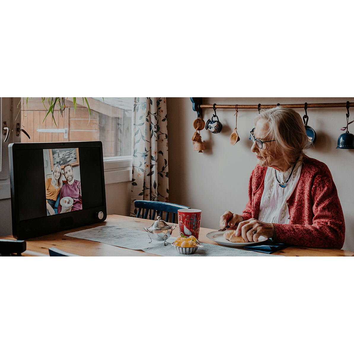 Eldre kvinne sitter ved kjøkkenbordet og snakker med familien på Komp (Foto: NO Isolation)