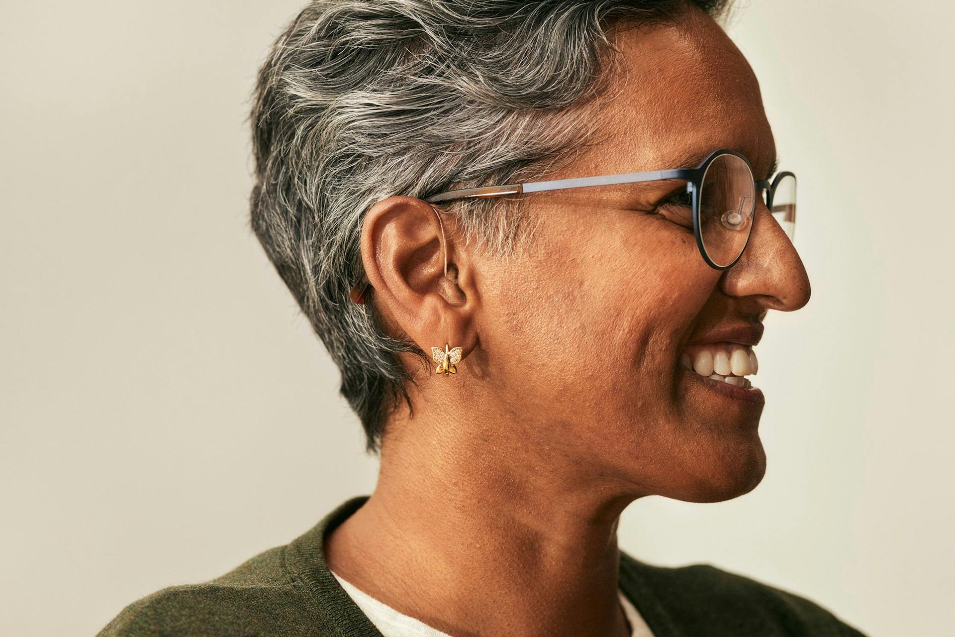 Kvinne med kort hår og briller i profil med høreapparater