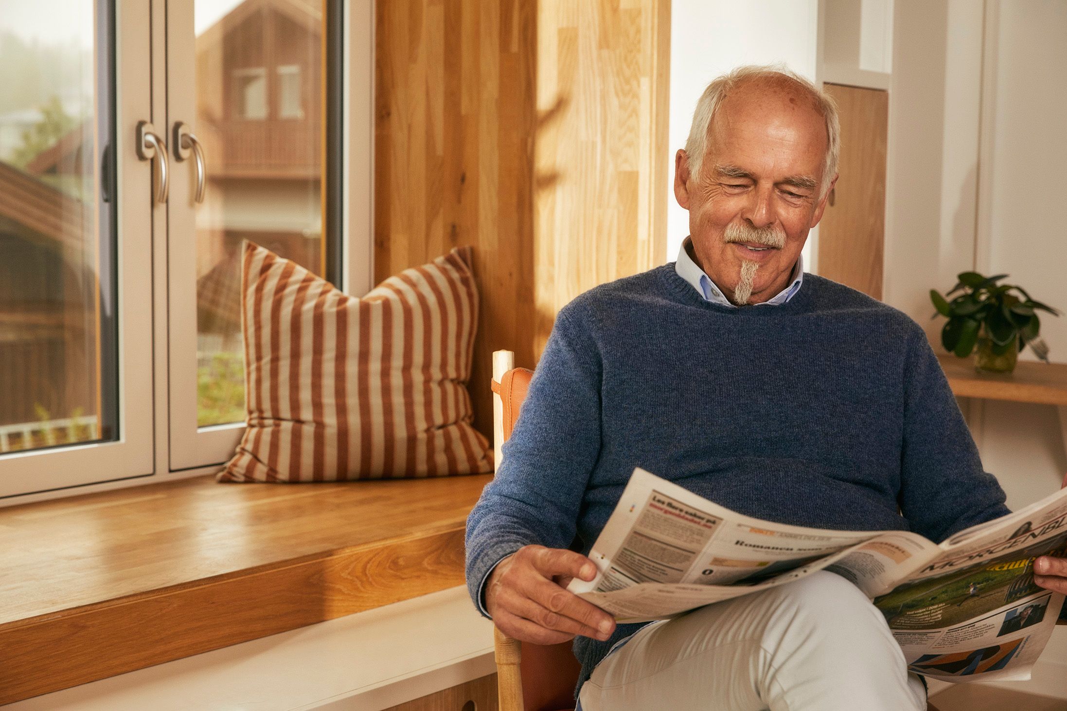 Bilde av smilende voksen mann med hvit bart og flippskjegg som leser avisen
